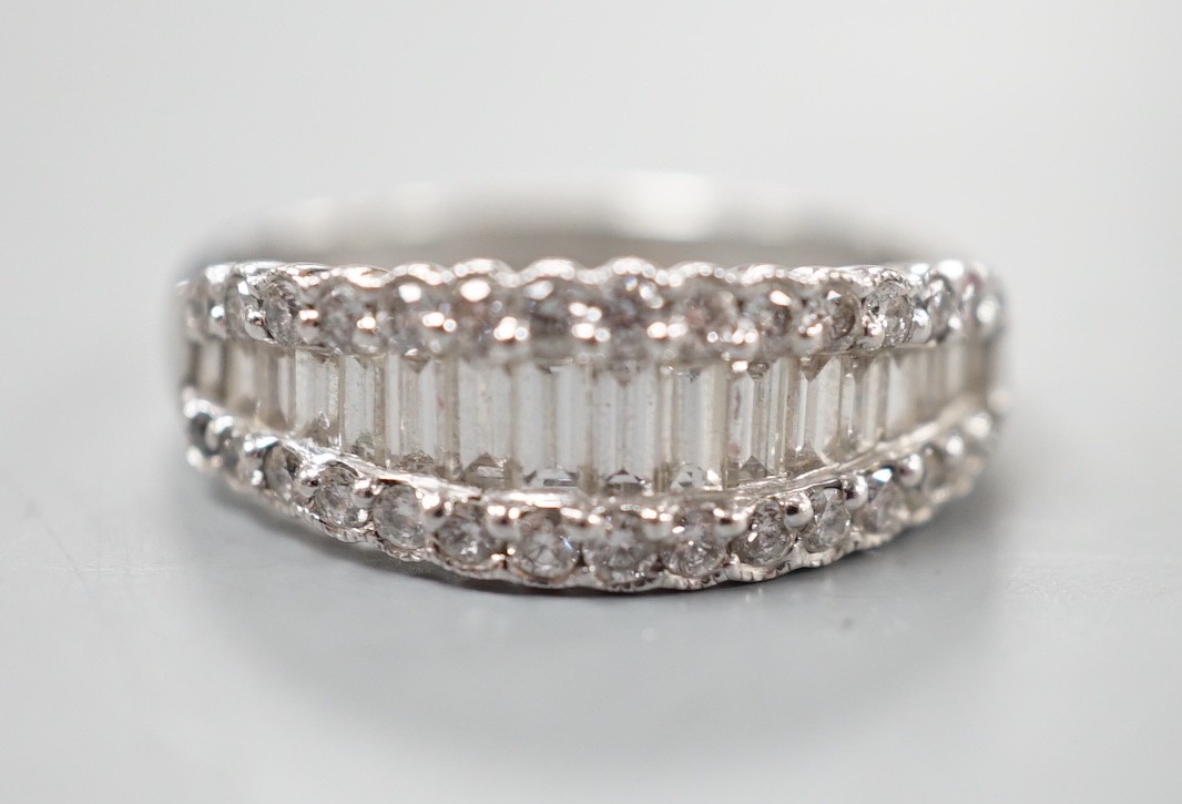 A modern white metal, graduated baguette cut diamond set half hoop ring, with diamond chip borders, size O, gross weight 5 grams.